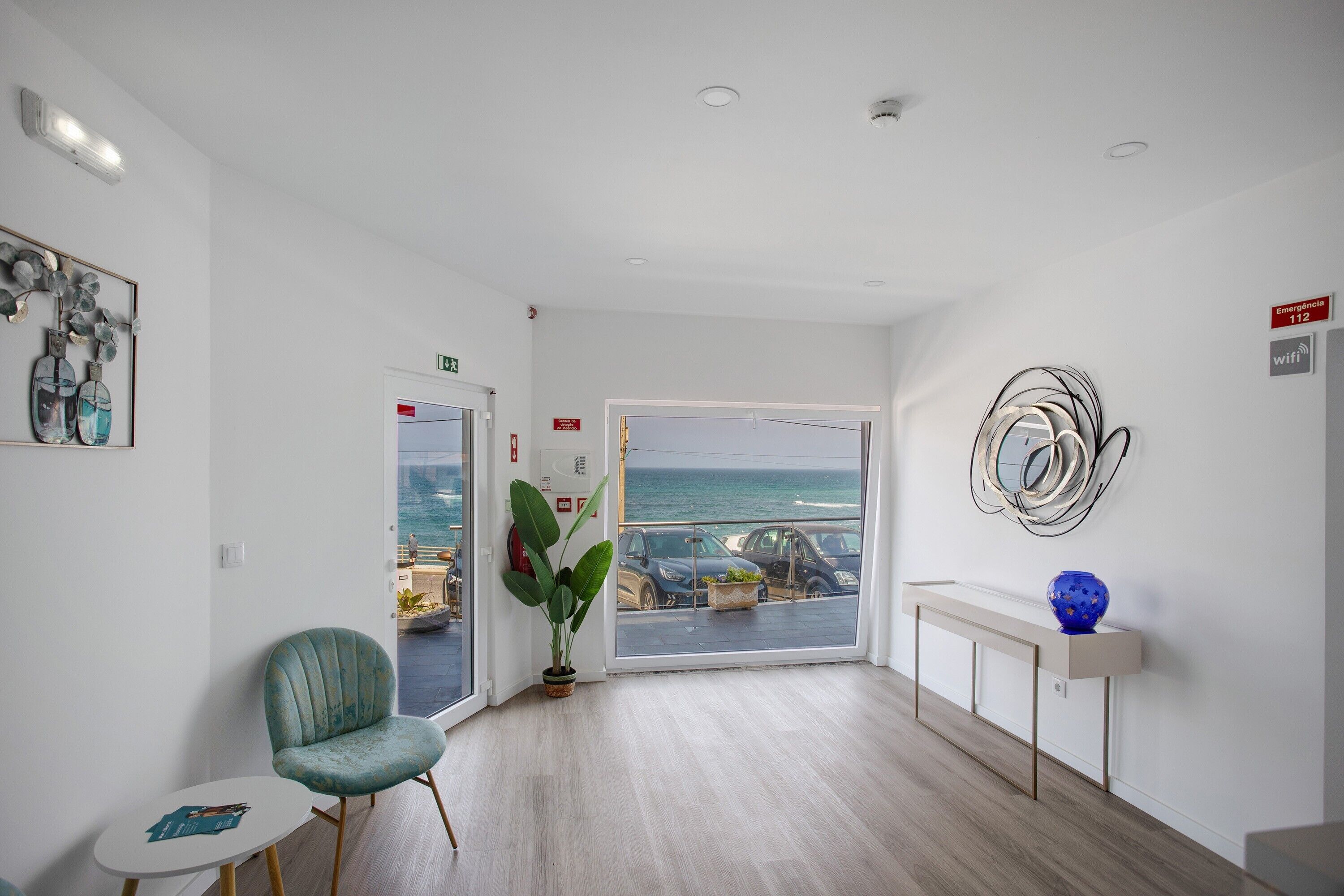 Een modern interieur met een zithoek, een plant, uitzicht op de oceaan en een decoratief object aan de muur.