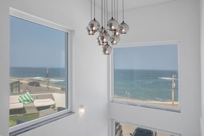 Une pièce dotée d’une grande fenêtre donnant sur l’océan, d’un luminaire suspendu et offrant une vue sur la plage.