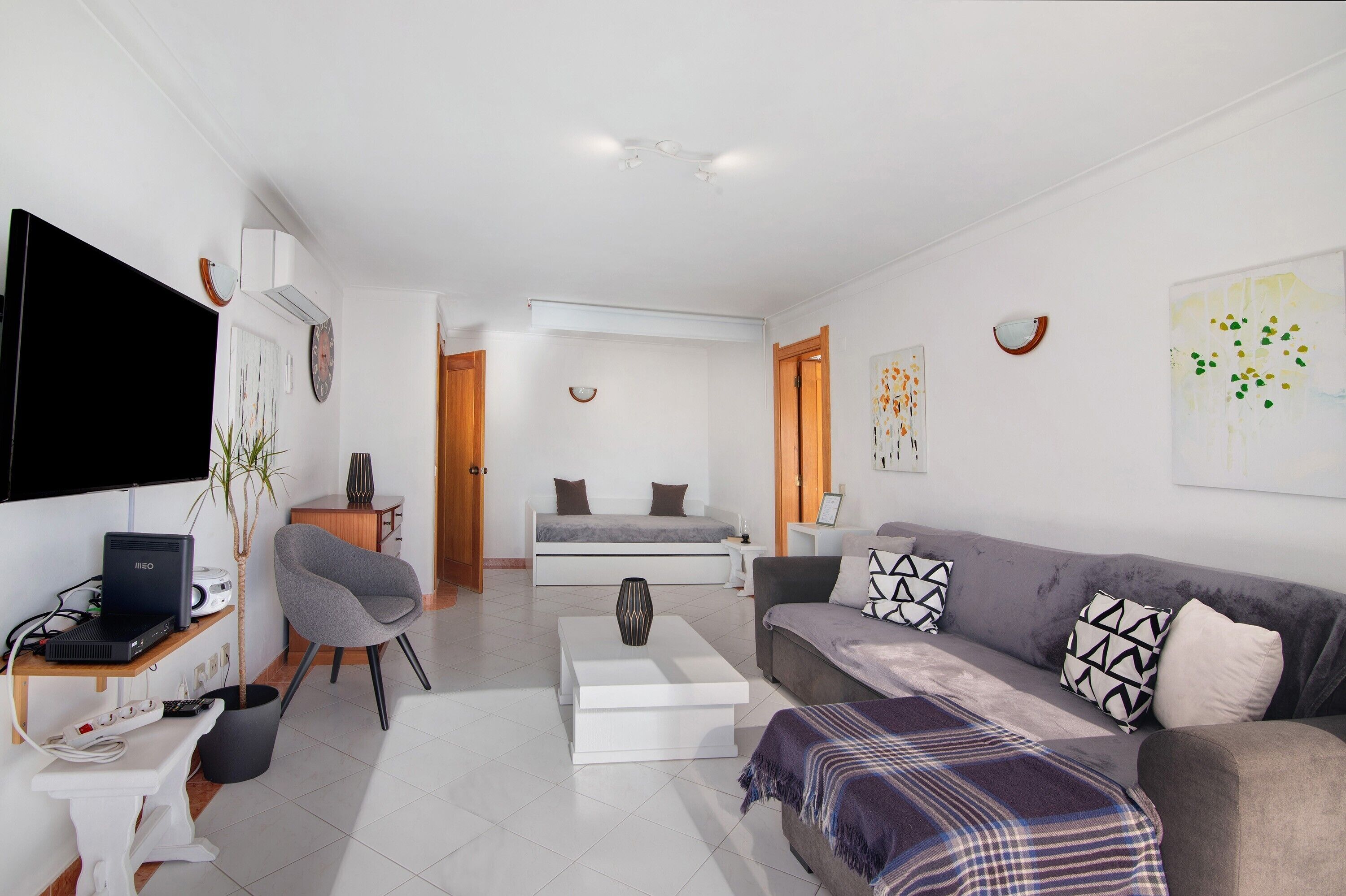A modern living room with a flat-screen TV, a sofa, a coffee table, and a dining area with a table and chairs.