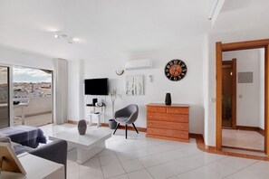 Un salon moderne avec une télévision, une horloge, un canapé, une table basse et une vue sur la ville.