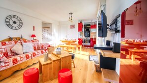 Uma sala de estar moderna com sofá, pufes e um espaço de jantar com mesas e cadeiras.