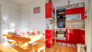 Uma cozinha compacta com armários vermelhos, uma mesa de jantar de madeira e uma pia de aço inoxidável.