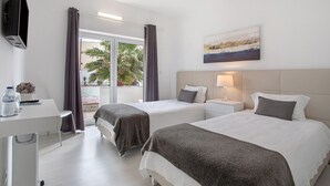 Une chambre d’hôtel avec deux lits, un bureau, une télévision, un tableau et une vue sur des palmiers.