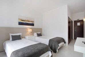 Une chambre d’hôtel avec deux lits, une table de chevet avec une lampe, un tableau au mur et une porte avec un panneau indiquant la sortie.