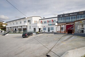 Un bâtiment moderne avec une enseigne indiquant « Mar do Norte », un espace extérieur abrité avec des sièges, et un parking.