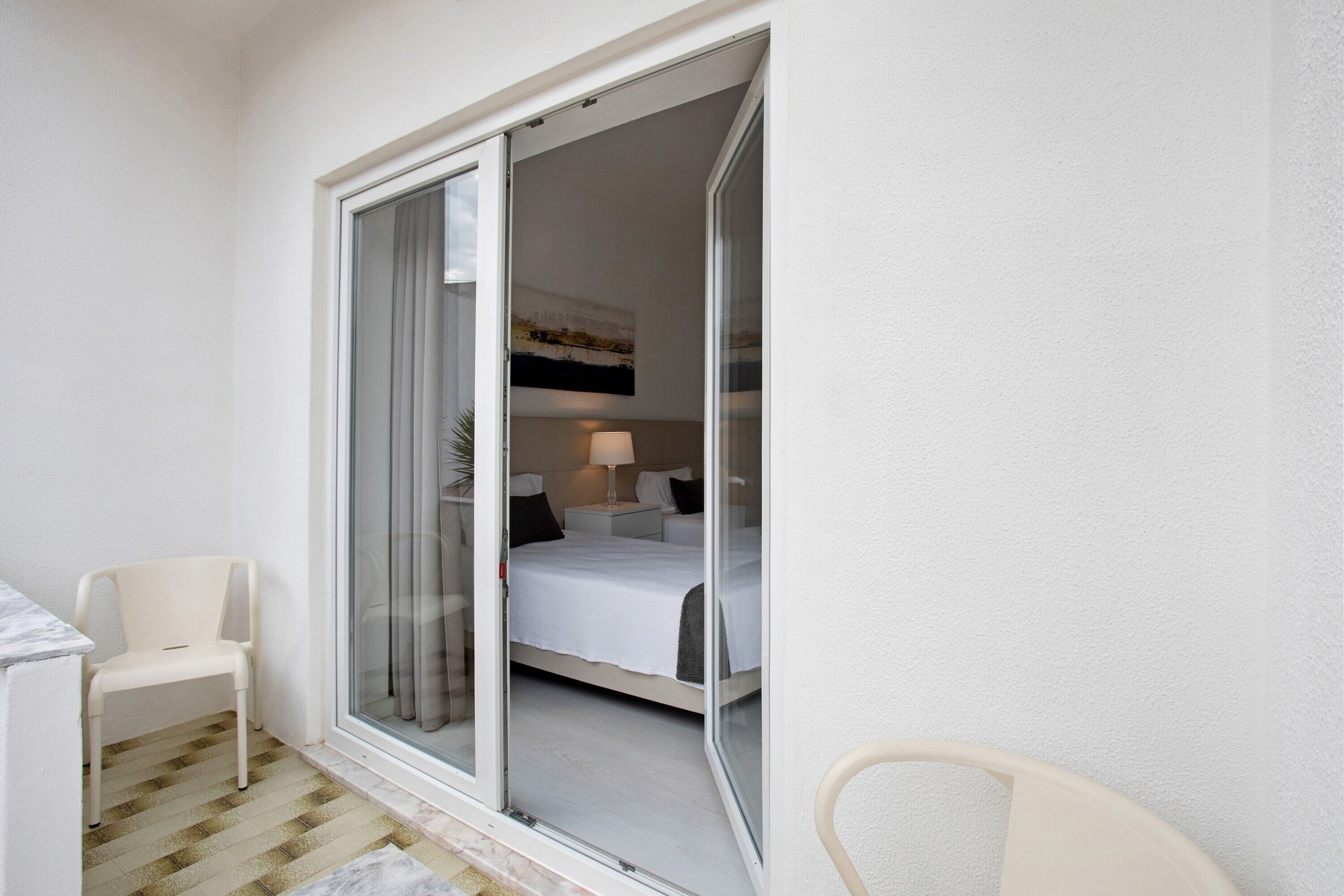 A room with a bed, a chair, and a sliding glass door leading to a balcony.
