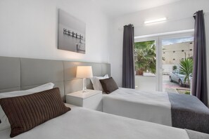 Habitación de hotel con dos camas, una mesita de noche con lámpara, una obra de arte en la pared y vista a la calle.