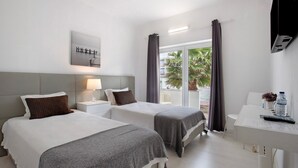 Quarto de hotel com duas camas, uma escrivaninha, uma cadeira, televisão e janela com cortinas.