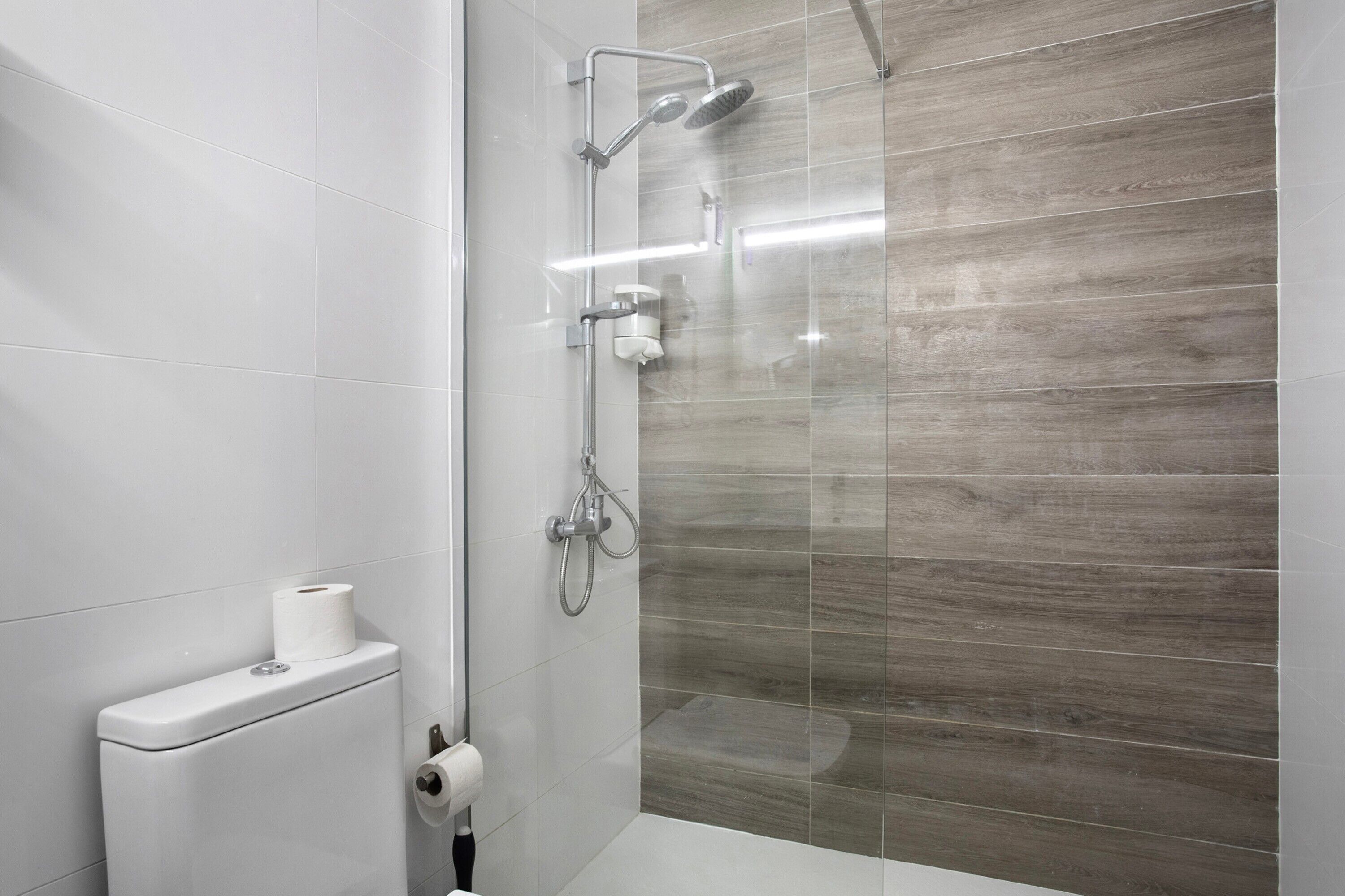 A modern bathroom with a toilet, a shower with a glass enclosure, and a toilet paper holder.