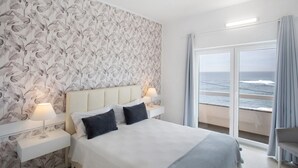 Ein Hotelzimmer mit Bett, Nachttischen, einer Lampe, Meerblick und einem Balkon mit Vorhängen.