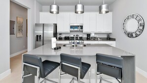 A modern kitchen with white cabinets, stainless steel appliances, and a central island with bar stools. - Modern, Luxury 1st Floor Condo Near Disney (Reunion)