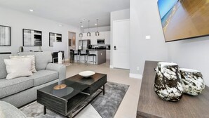 A modern living room with a grey sofa, a coffee table, and a kitchen in the background. - Modern, Luxury 1st Floor Condo Near Disney (Reunion)