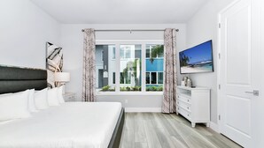 A bedroom with a bed, a nightstand, a dresser, a TV, and a window with curtains. - Modern, Luxury 1st Floor Condo Near Disney (Reunion)