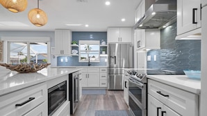 Une cuisine moderne avec des meubles blancs, des appareils en acier inoxydable et un grand îlot central.
