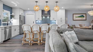Une cuisine moderne avec des meubles blancs, un îlot central et des chaises en osier.
