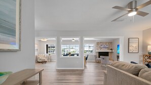 A spacious living room with a large sofa, a wooden coffee table, and a ceiling fan. There are large windows providing natural light and a view of the outdoors. - ⚓Sandys Coral Retreat! Canal Front, Pool, Hot Tub & More⚓ (Bradenton)