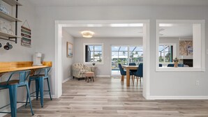 A spacious kitchen with a wooden countertop and blue bar stools, a dining area with a table and chairs, and large windows offering views of the outdoors. - ⚓Sandys Coral Retreat! Canal Front, Pool, Hot Tub & More⚓ (Bradenton)