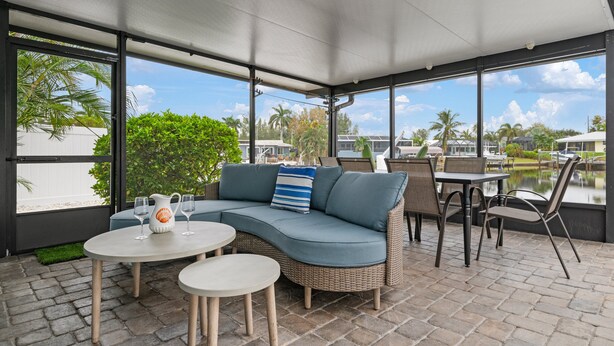 A covered outdoor seating area with a wicker sofa, two round tables, and chairs. - ⚓Sandys Coral Retreat! Canal Front, Pool, Hot Tub & More⚓ (Bradenton)