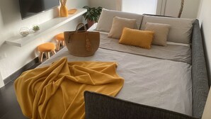 A modern living room with a sofa, a flat-screen TV, a plant, and a basket. - The Yellow House (Scardovari)