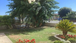 A landscaped garden with a palm tree, red flowers, and a seating area with chairs and a table. - The Yellow House (Scardovari)