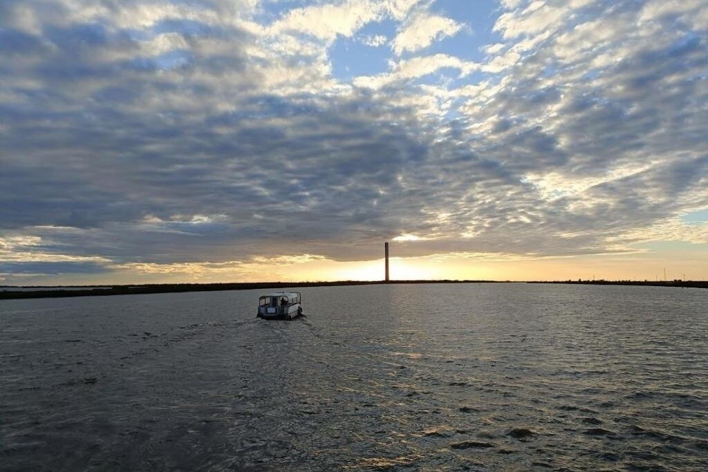 Un barco sobre aguas tranquilas con un atardecer y nubes al fondo.