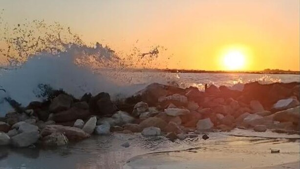 A sunset over a rocky shoreline with waves crashing against the rocks. - The Yellow House (Scardovari)