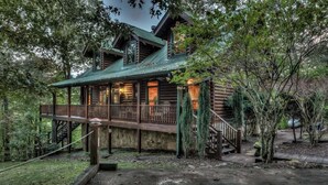 Une cabane rustique en rondins de bois, dotée d’une terrasse en bois, d’un escalier menant à l’étage supérieur et d’un porche aménagé avec des sièges.
