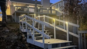 A wooden staircase leading to a deck with railings, surrounded by trees and a house in the background. - Lakefront escape! Boat Dock, Fishing, Kayaks! Near Hiking, Wineries, Marinas!! (Creal Springs)