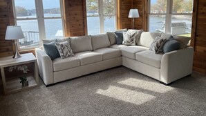 A cozy cabin with a beige sectional sofa, a lamp on a side table, and large windows overlooking a lake. - Lakefront escape! Boat Dock, Fishing, Kayaks! Near Hiking, Wineries, Marinas!! (Creal Springs)