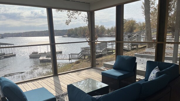 A covered outdoor seating area with wicker furniture and a view of a lake with boats. - Lakefront escape! Boat Dock, Fishing, Kayaks! Near Hiking, Wineries, Marinas!! (Creal Springs)