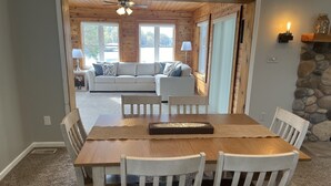 A dining area with a wooden table and chairs, a sofa in the background, and a stone wall. - Lakefront escape! Boat Dock, Fishing, Kayaks! Near Hiking, Wineries, Marinas!! (Creal Springs)