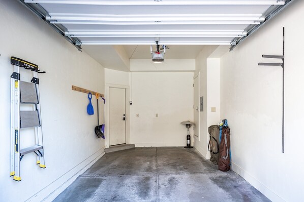 A garage with a concrete floor, a ladder, a blue paddle, and a bag hanging on the wall.