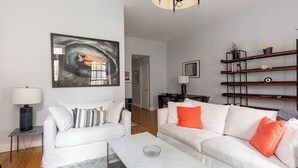 Een moderne woonkamer met twee witte banken, een marmeren salontafel en een boekenkast met boeken en decoratieve objecten.