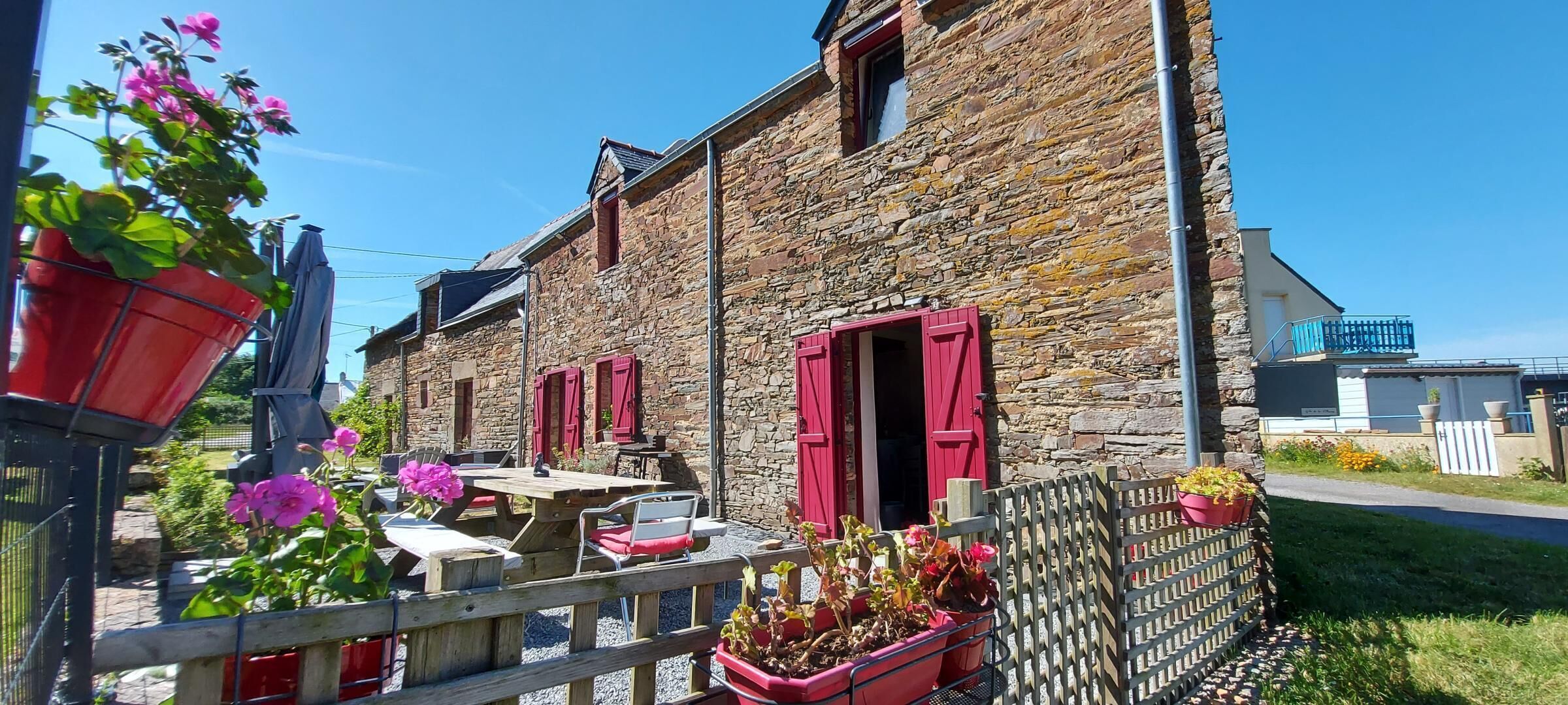 A stone building with red shutters, outdoor seating, and potted plants.