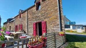 A stone building with red shutters, outdoor seating, and potted plants. - Maison de la Vilaine (SAINT DOLAY)