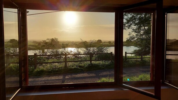 A room with a large sliding glass door leading to a scenic outdoor view of a lake and surrounding greenery. - Maison de la Vilaine (SAINT DOLAY)