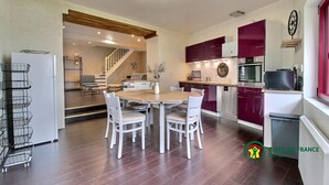 A modern kitchen with a dining area, featuring a round wooden table and white chairs, a built-in oven, and a microwave. - Maison de la Vilaine (SAINT DOLAY)