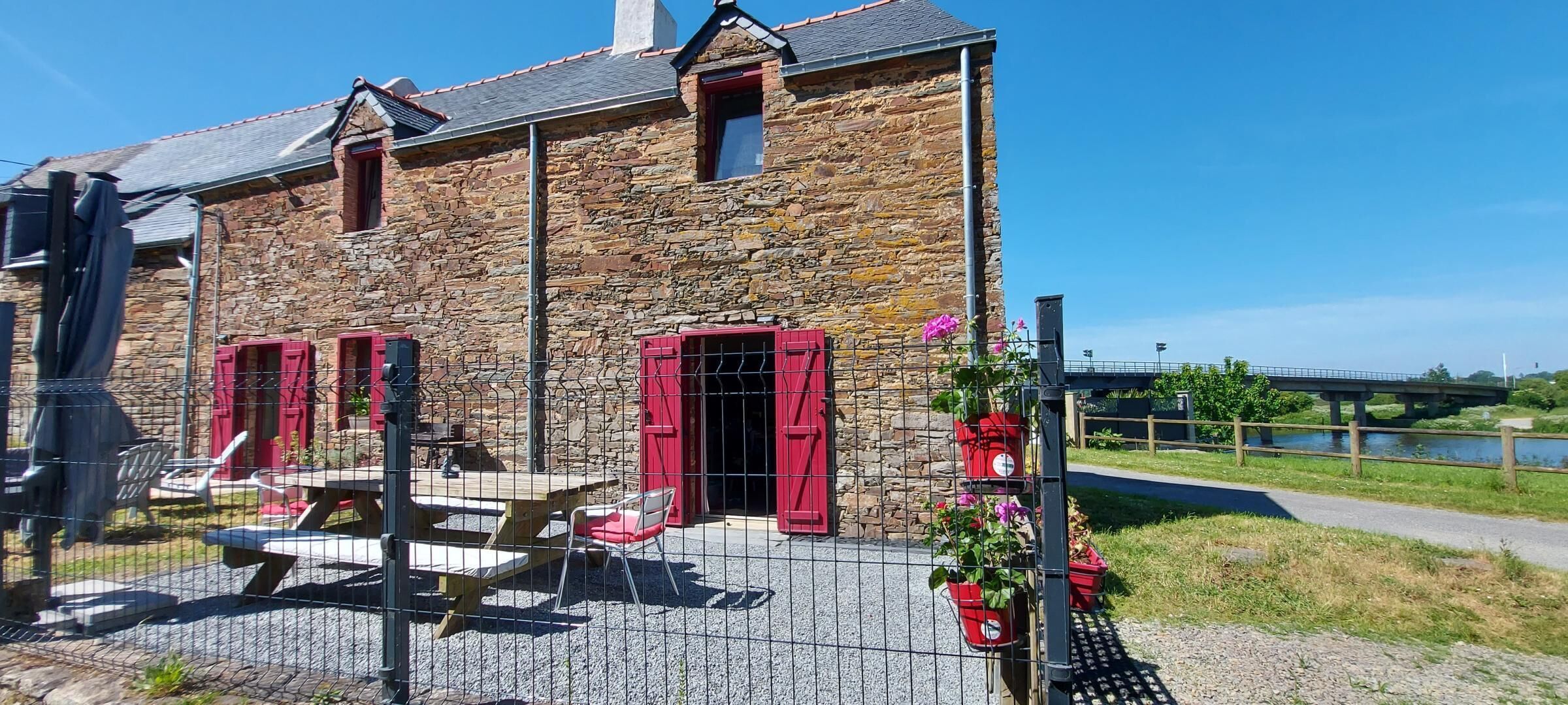 Een stenen gebouw met rode luiken, een picknicktafel en een hek.