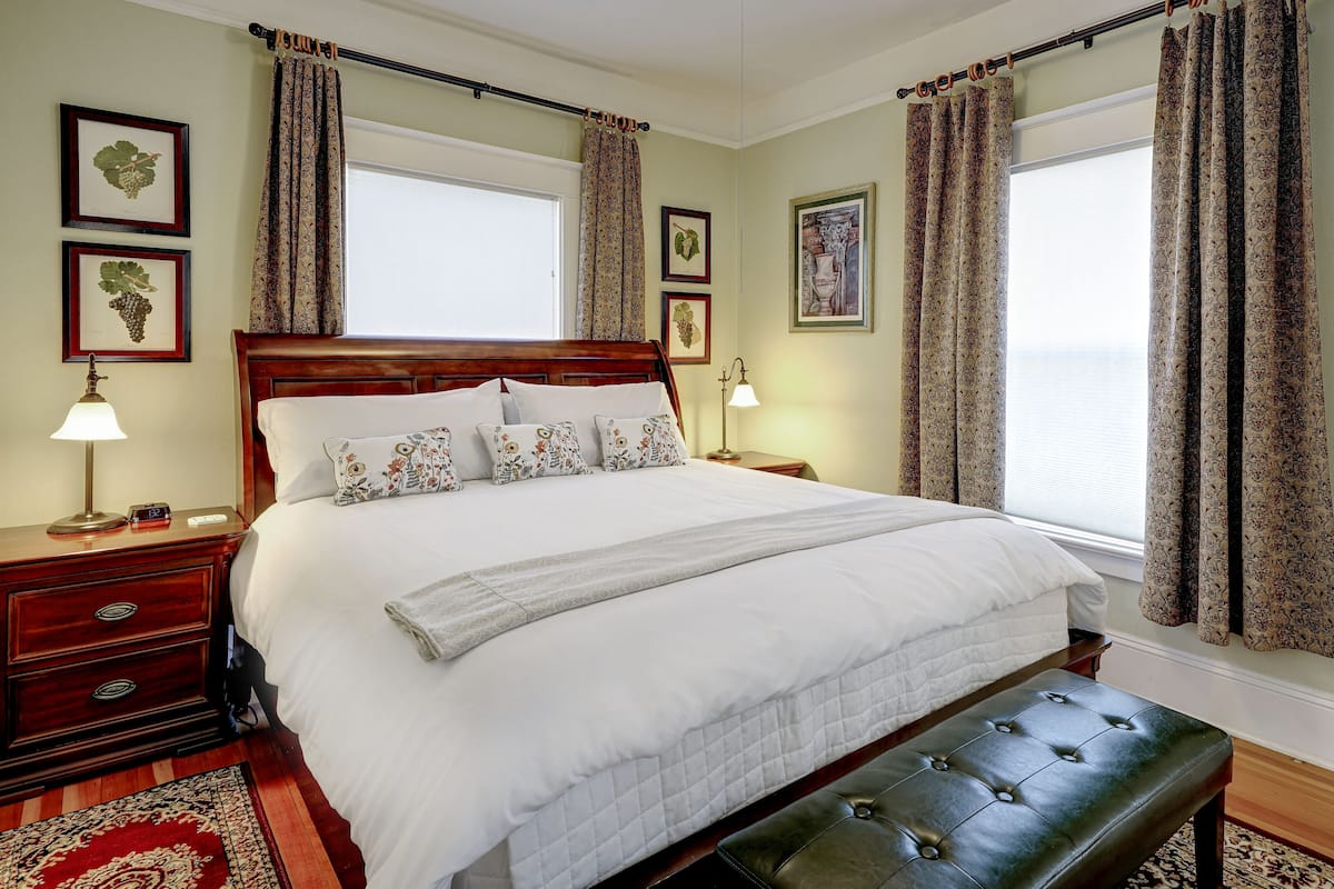 Een netjes opgemaakt slaapkamer met een groot bed, een nachtkastje met lamp en een bankje.