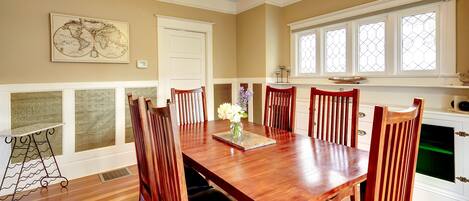 A dining room with a wooden table, six chairs, a vase with flowers, and a world map on the wall.