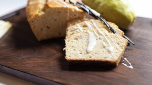Una porción de pastel con cobertura blanca y un palito de vainilla sobre una tabla de madera.