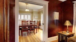 Un comedor con sillas de madera y una mesa, una lámpara sobre una mesita auxiliar y una puerta que da a otra habitación.