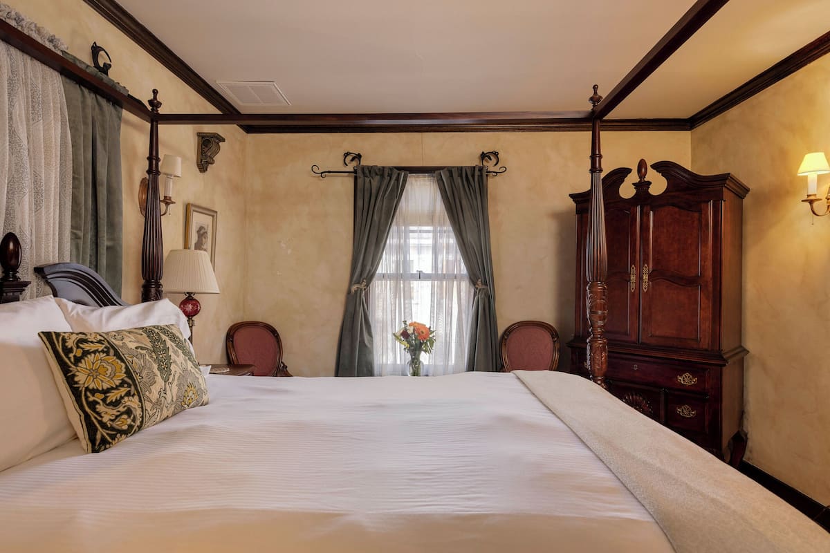 Een hotelkamer met een groot bed, een houten garderobe, een bureau met een lamp en een raam met gordijnen.