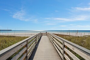 Una passerella in legno che conduce a una spiaggia sotto un cielo sereno.