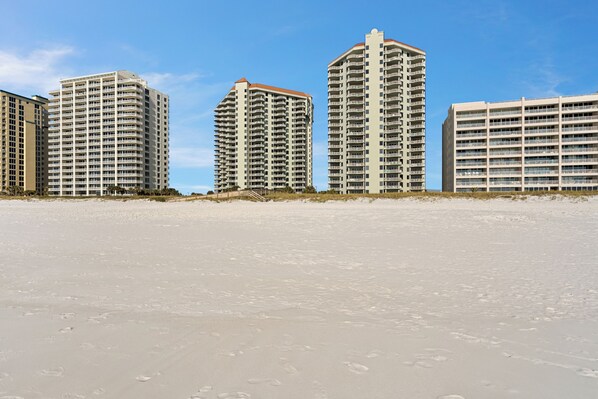 Um hotel à beira-mar com vários edifícios altos, praia arenosa e céu azul límpido.
