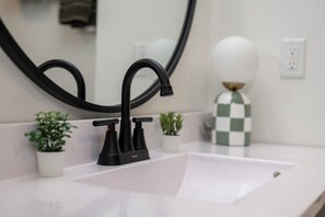 Un baño moderno con un grifo negro, un lavabo blanco y dos pequeñas macetas con plantas.