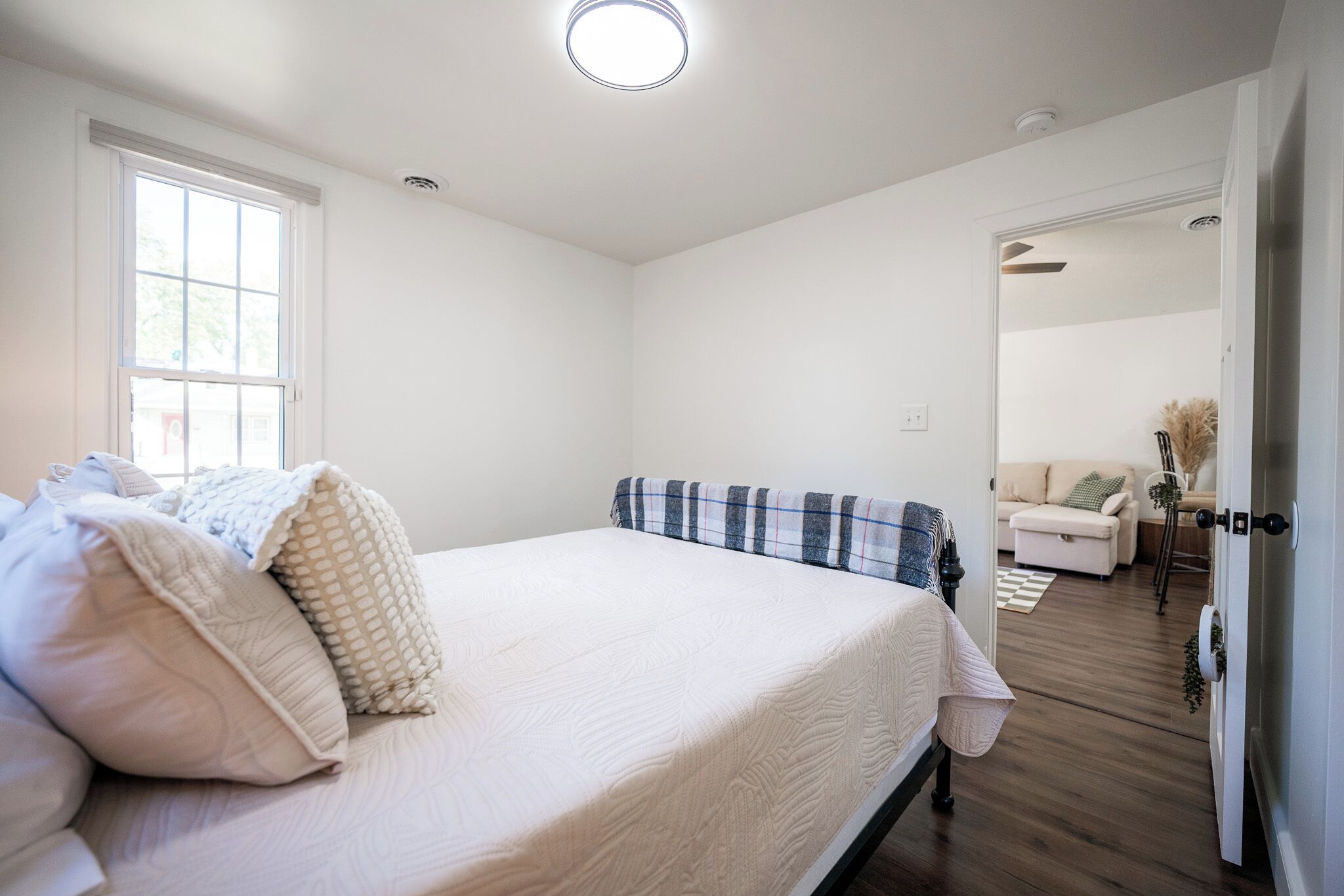 A bedroom with a large bed, a window, and a door leading to another room.