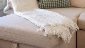 A beige sofa with a white throw blanket and a green checkered pillow. - Core's Cottage: Fountain Square- Cozy 1BR Dwtn Indy (Indianapolis)