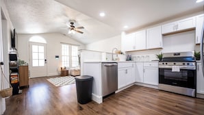 A modern kitchen with white cabinets, stainless steel appliances, and a wooden floor. - Core's Cottage: Fountain Square- Cozy 1BR Dwtn Indy (Indianapolis)