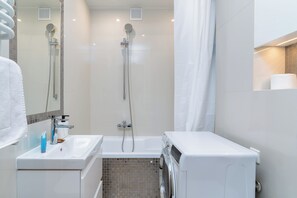 Ein modernes Badezimmer mit Dusche, Waschbecken und einer integrierten Waschmaschine.